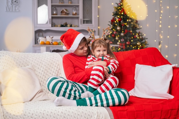 Christmas time. cute kids brother and sister in Christmas pajamas hugging together on couch