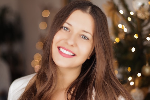 Christmas time and holiday mood concept happy smiling woman and decorated xmas tree lights on backgr...