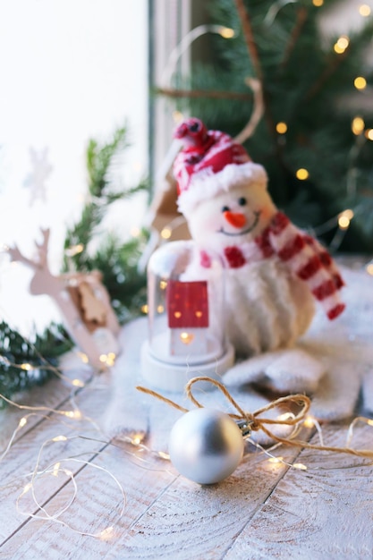 Christmas toys a snowman and a house balls spruce branches illumination on a wooden windowsill