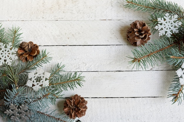 Christmas tree branch with snowflakes and pine cones on white wooden background with copy space