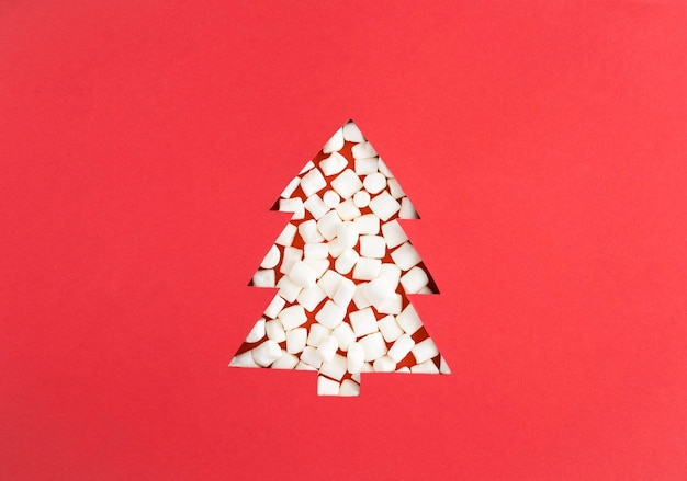 Christmas tree cut out on the red background and filled with marshmallows Closeup Copy space