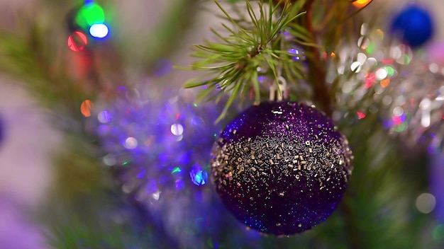 Christmas tree decorated with blue glass ball on christmas spruce branch on background bokeh of flickering light bulbs garlands