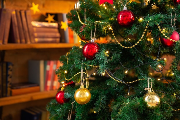 Christmas tree decorated with garlands and balls against background of library bookshelves