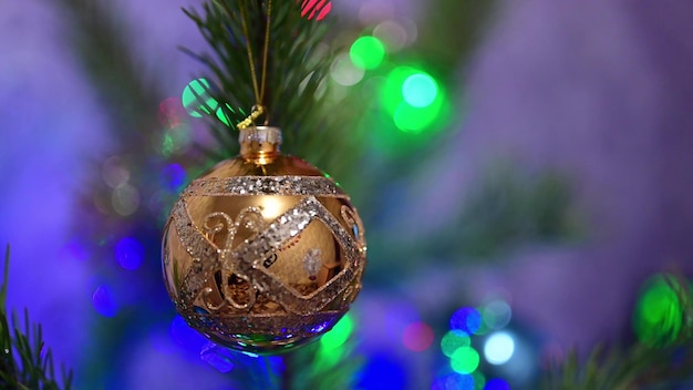 Christmas tree decorated with golden glass ball on christmas spruce branch on background bokeh of flickering light bulbs garlands