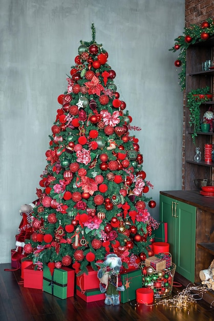 Christmas tree decorated with red and green balls, toys and ornates in a dark interior. New Year fir tree decorated with the gifts and bright boxes. Vertical shot.