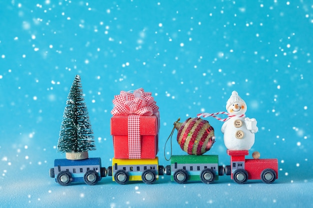 Christmas tree and gift box, ball and snowman on toy train on blue