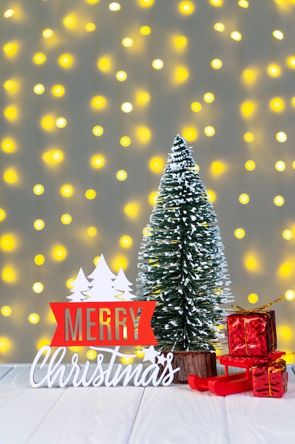 Christmas tree gift boxes and wooden lettering Merry Christmas on light bokeh background