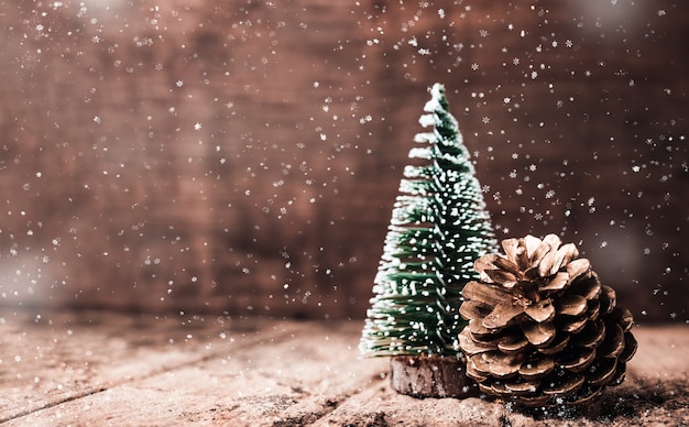 Christmas tree and gold pine cone and snow falling on grunge wood table 