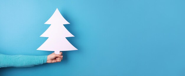 Christmas tree in hand over blue background, panoramic layout