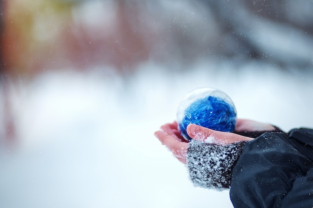 Photo christmas tree in the hands of a child. round blue christmas ball on snow background.