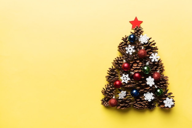 Christmas tree made from natural cones on colored background, view from above. New Year minimal concept with copy space