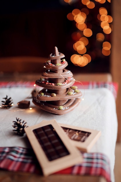 Christmas tree made of natural chocolate stands on the festive table against the background of lights, cozy home atmosphere