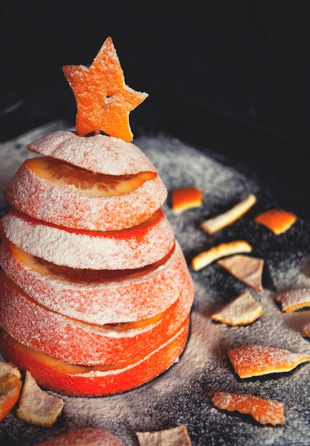 Christmas tree made of sliced orange sprinkled with powdered sugar next to orange peels.