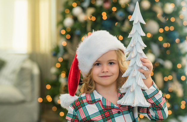 Photo christmas tree portrait of a little child boy in christmas santa hat child preparing for the new year or christmas holidays