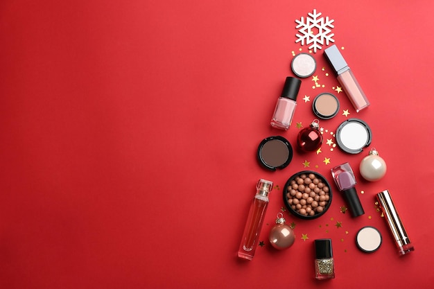 Christmas tree shape of decorative cosmetic products on red background flat lay with space for text Winter care