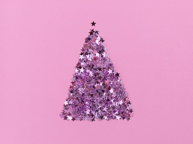 Christmas tree shape from confetti stars on a pink paper. Festive monochrome flat lay.