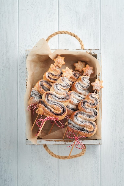 Christmas tree shape puff pastry cakes with chocolate filling sugar powder and lollipops on old white wooden background Christmas New Year Appetizer Festive idea for Christmas or New Year dinner