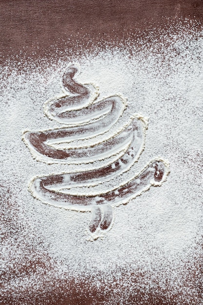 Christmas tree silhouette made of flour on a dark brown background. New Year's card idea