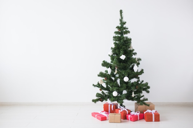 Christmas tree with balls and gift boxes over white wall with copy space