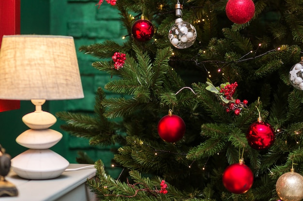 Christmas tree with red balls and lamp on green wall background. Photo