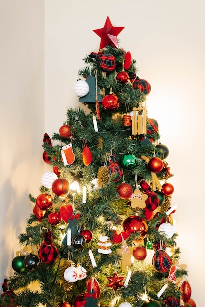 Christmas tree with red toys and green ones on a light wall background