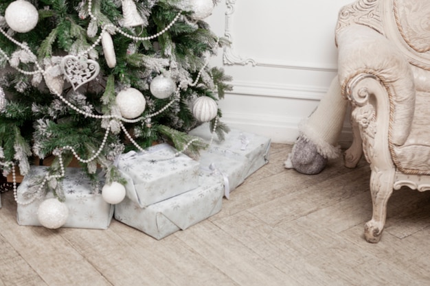 Christmas tree with silver toys on a derelict floor in the interior. Gifts in gift wrapping. New Year celebration. Close-up. Blurred.