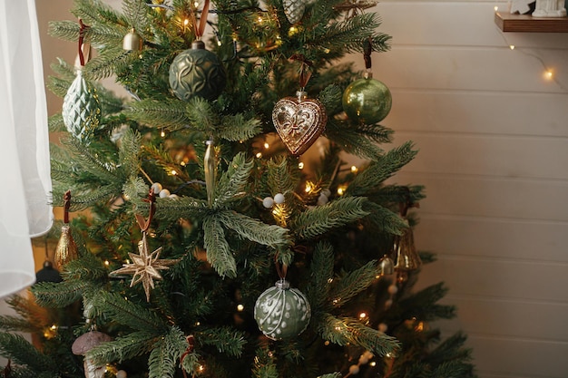 Christmas tree with vintage baubles and golden lights close up Modern decorated christmas tree branches with stylish ornaments in festive room Winter holidays atmospheric time