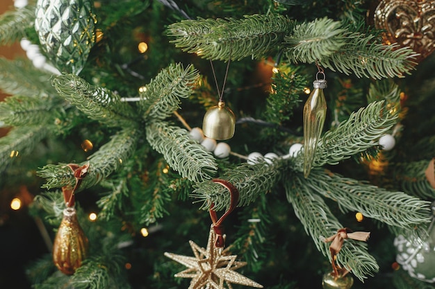 Christmas tree with vintage baubles and golden lights close up Modern decorated christmas tree branches with stylish ornaments in festive room Winter holidays preparation atmospheric time