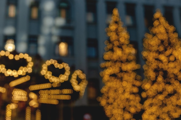 Christmas trees and carousel in christmas light garland on background of multi storey building blurr...