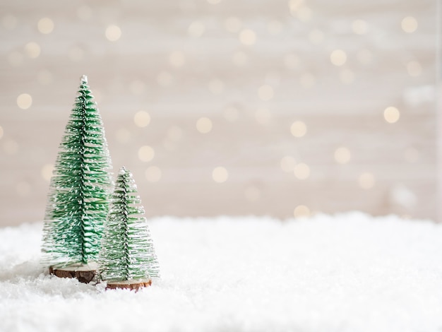 Christmas trees in the foreground in artificial snow with a glowing garland. Copy space.