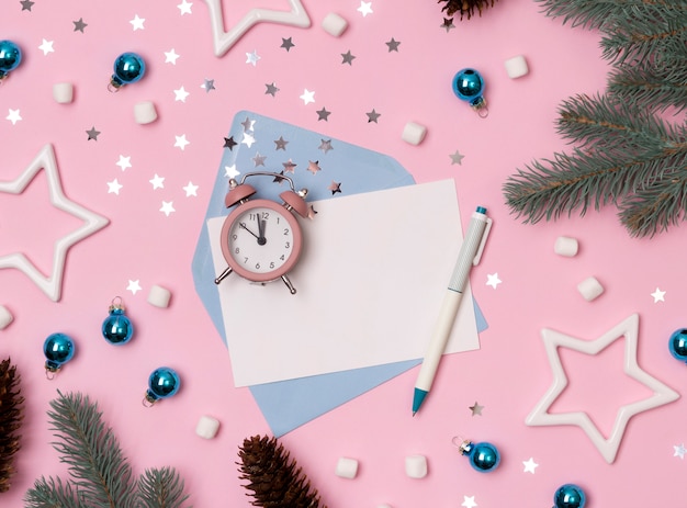 Christmas winter decorations, envelope with alarm clock, snowflakes and blank greeting card on pink background