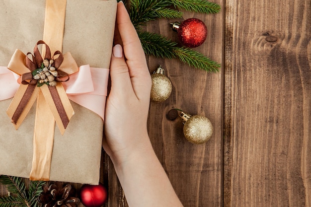 Christmas  with gift boxes, paper's rools and decorations on red. Preparation for holidays. Top view with copyspace. Woman's hands holding gift box