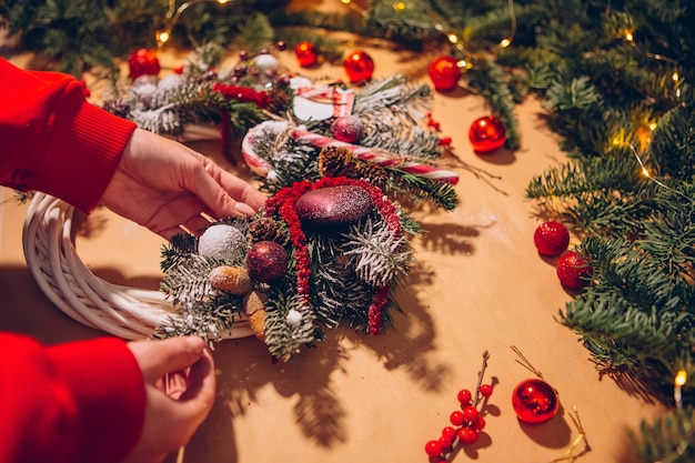 Christmas wreath, Female hands closeup makes a wreath of spruce and decorates with red balls,