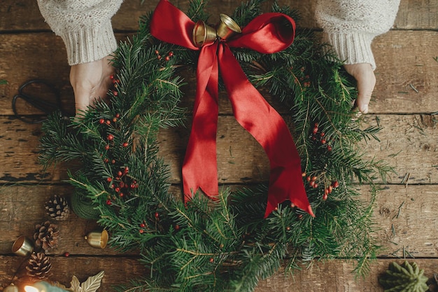 Christmas wreath flat lay Woman hands holding christmas wreath with red ribbon on rustic wood