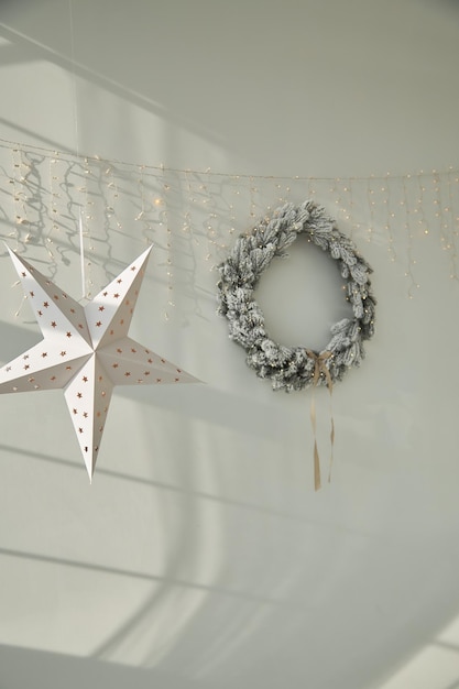 Christmas wreath spruce decorated with white snow balls candles lights garland on the wall in white interior