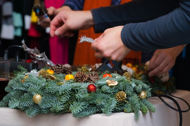 Christmas wreath weaving workshop. Woman hands decorating holiday wreath made of spruce branches, cones and various organic decorations on the table