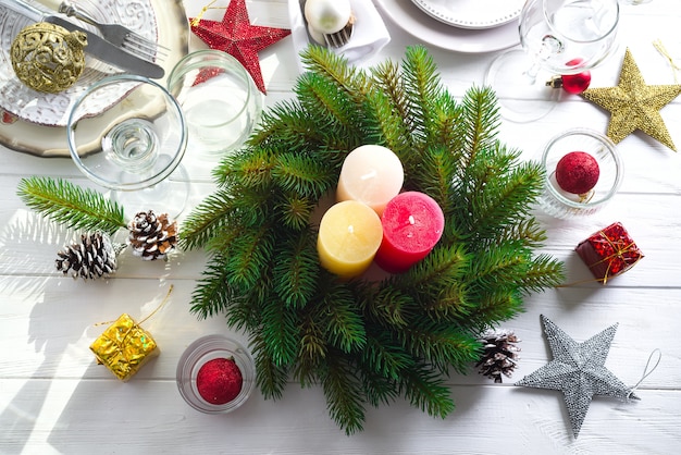 Christmas wreath with colorful big candles on a table with a Christmas table setting 