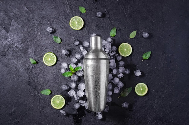 Chrome Bar Shaker With Lime Mint and Ice on Dark Stone Table Concept Of Cold Summer Drinks Top View Flat Lay Copy Space For Your Text