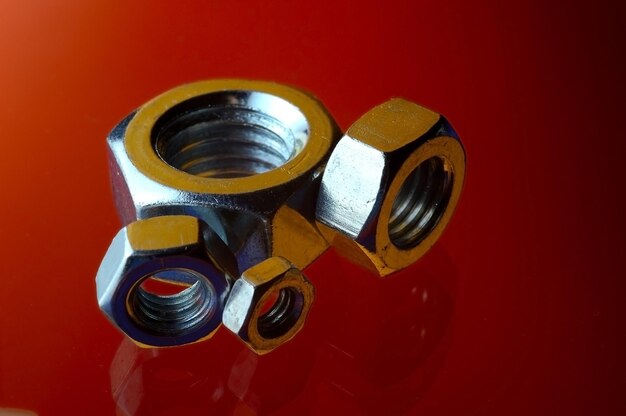 Chrome-plated metal nuts of different sizes, highlighted in different colors, laid out on a red background.