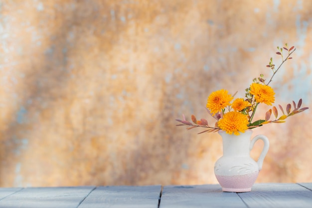 Chrysanthemum flowers in jug on background old wall in sunlight