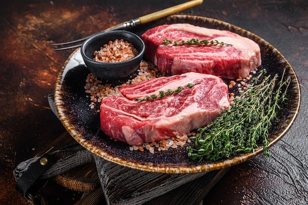 Chuck eye Roll beef steaks raw meat on a plate with thyme and herbs Dark background Top view