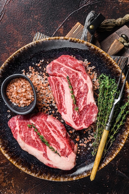 Chuck eye Roll beef steaks raw meat on a plate with thyme and herbs Dark background Top view