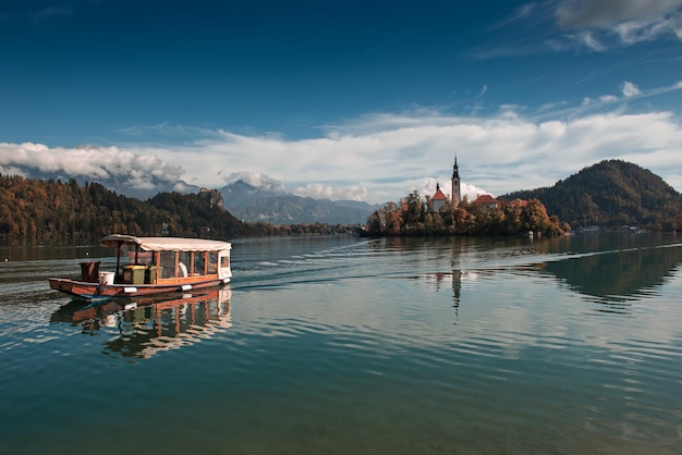 Church of Assumption in Lake Bled Slovenia with blue sky touristic boat and clouds in the autumn