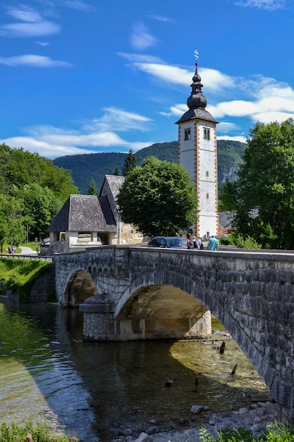 Church on the shore of a mountain lake and an old stone bridge over the river.