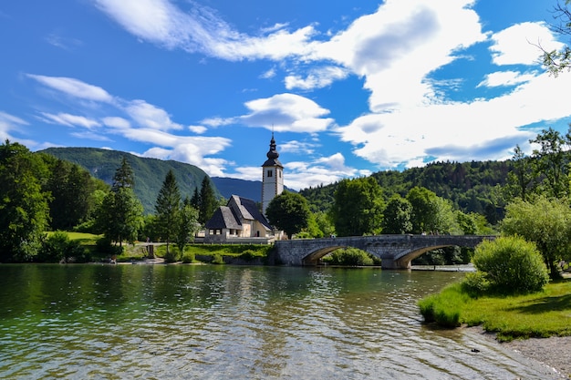 Church on the shore of a mountain lake and an old stone bridge over the river.