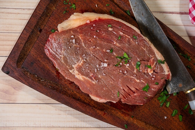 Churrasco de cuadril or raw steak on a rustic wooden cutting board with herbs. Top view.