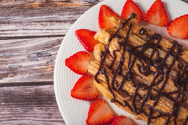 Churros with chocolate and strawberries on a white plate.