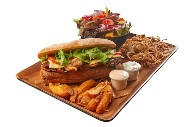 Ciabatta Grilled Chicken Sandwich with Lettuce Cheese and Tomato on Wood Plate With Potato Wedges and a Salad Bowl with Mayonnaise Spicy Sauce and Fried Onions Isolated