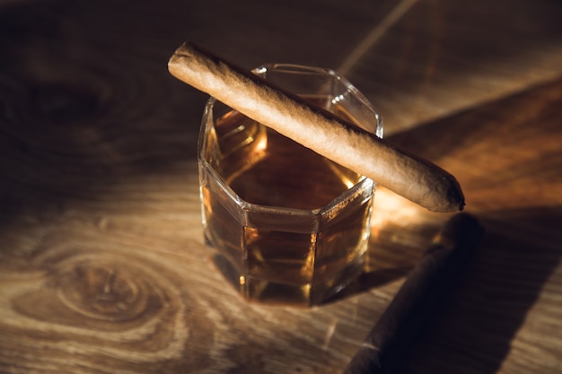 Cigar on a glass of whiskey on the table