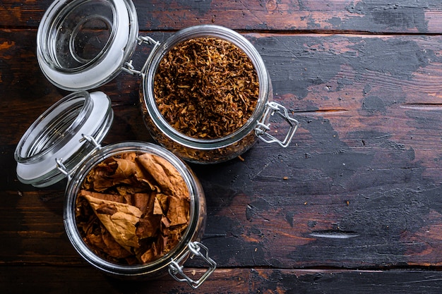 Cigar and pile of tobacco leaves of Dried tobacco  in glass jars on rustic wood dark table top view space for text